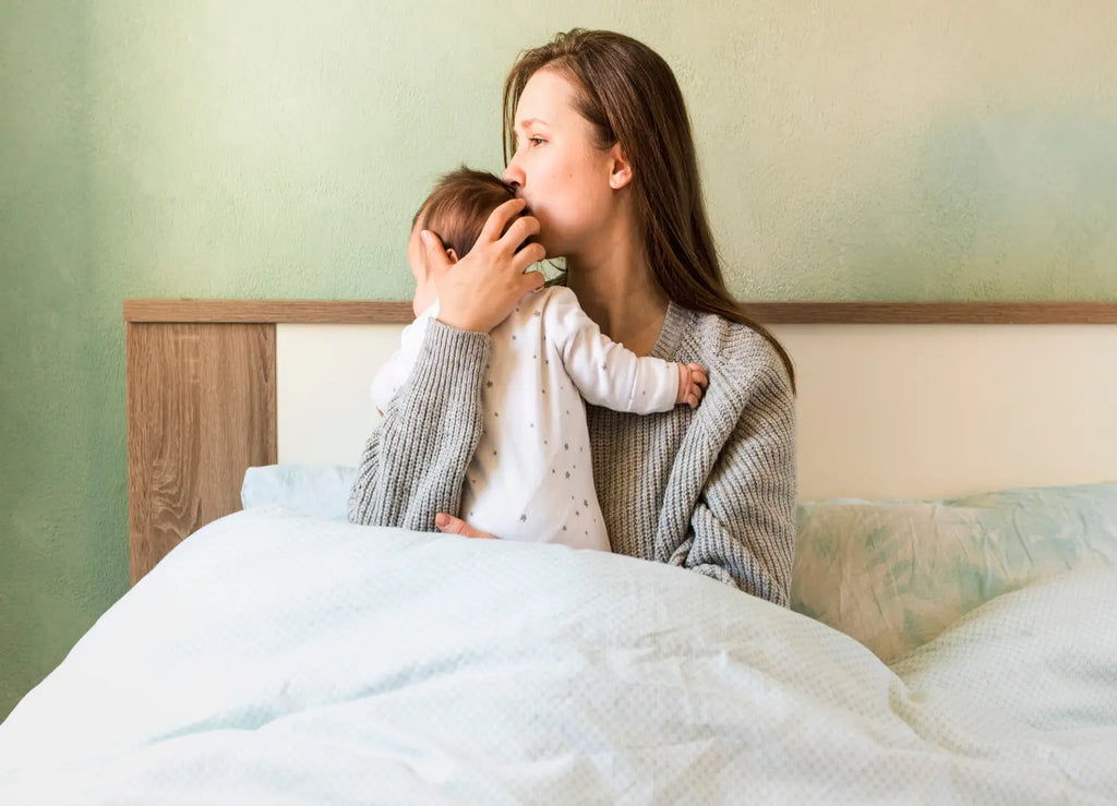 A mother kissing baby arms bed