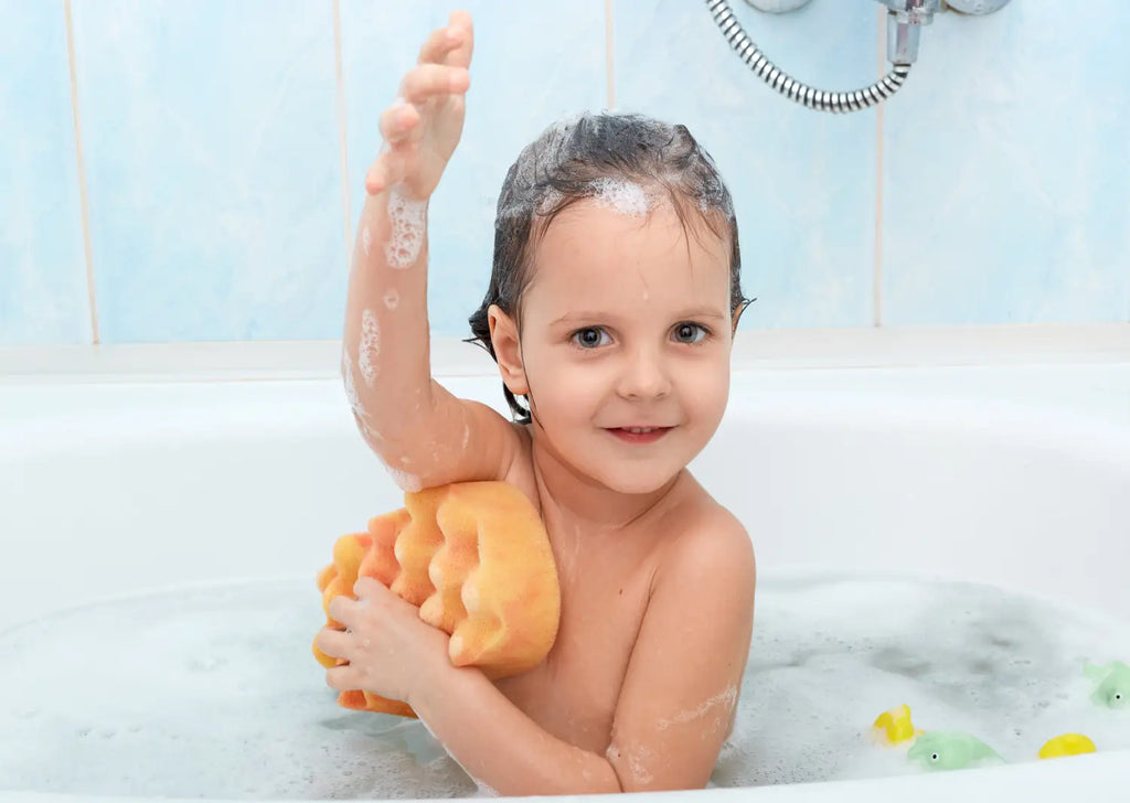 Cheerful positive adorable small child taking bath washing herself