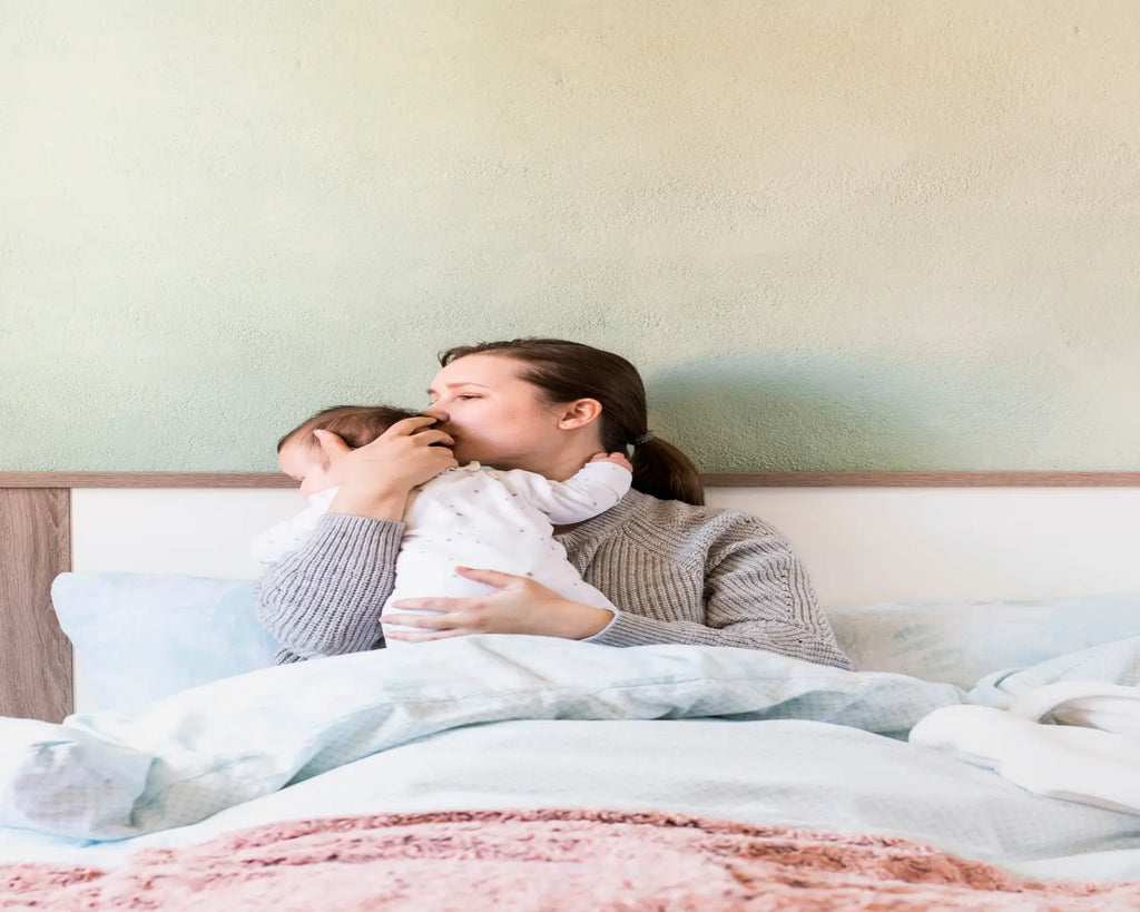 Woman kissing baby arms bed