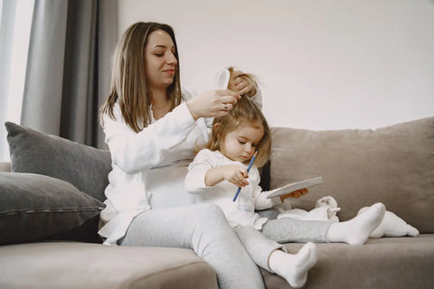 mom sitting couch ties her daughters'hair